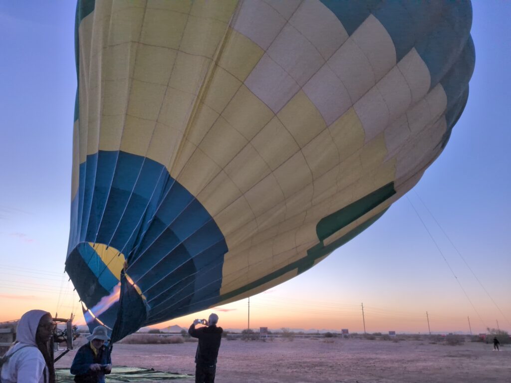 Hot-air balloon being inflated on the ground before sunrise, with the burner firing into the balloon envelope.