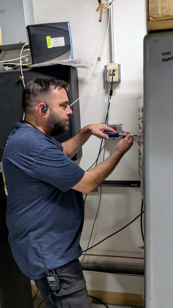 Josh Cavender, KE7WIL, checking equipment beside the NY7S repeater rack in the elevator machine room.