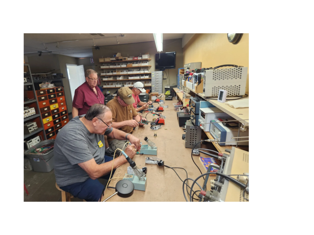 Amateur radio operators working on electronics and soldering projects at the West Valley Ham Shack workbench.